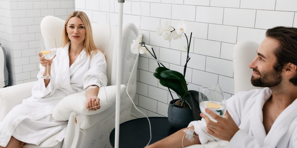 Couple in love during intravenous vitamin therapy. Beautiful woman with her boyfriend with glasses of refreshing drink with lemon in medical clinic for detox their organisms