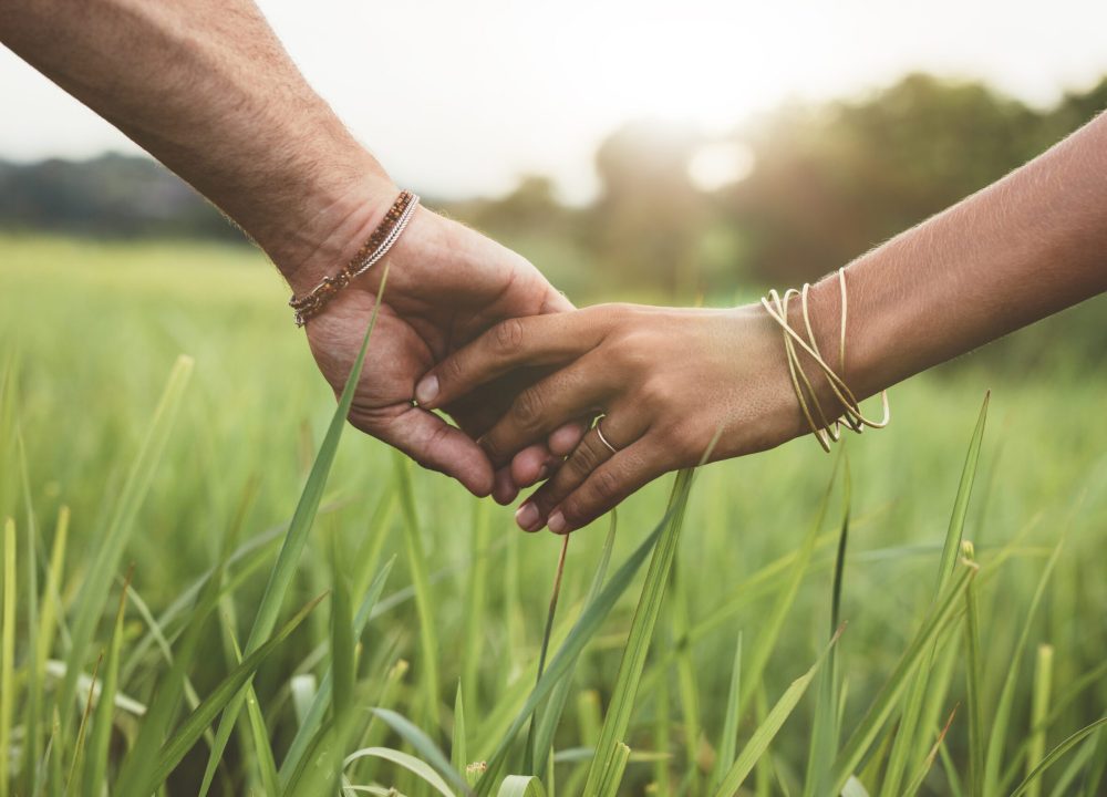 Shot of romantic couple holding hands in a field. Close up shot of man and woman with hand in hand walking through grass field.